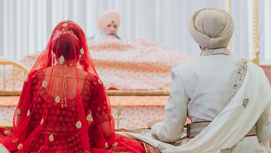 Sikh couple sitting in front of Guru Granth Sahib during Anand Karaj ceremony at Guru Gobind Singh Gurdwara in Bradford