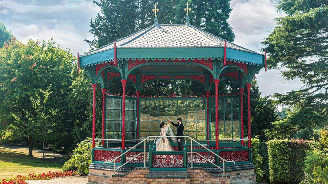 The couple is dressed in Asian Wedding attire, as they stand in the Subtropical Glasshouse, Birmingham Botanical Gardens for their Asian Wedding Photography. They are surrounded by lush greenery, including palm trees and other plants. 