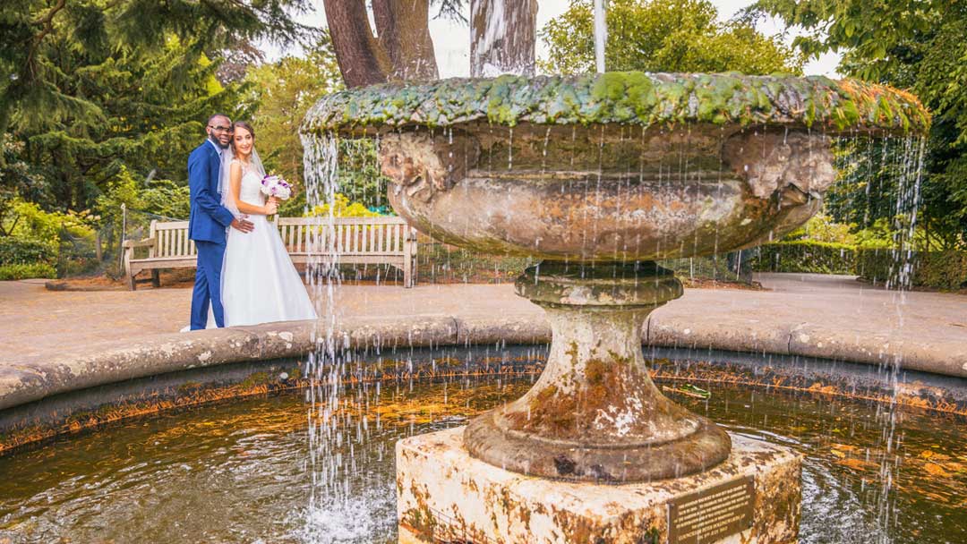 The couple is dressed in Asian Wedding attire, as they stand in the Subtropical Glasshouse, Birmingham Botanical Gardens for their Asian Wedding Photography. They are surrounded by lush greenery, including palm trees and other plants. 