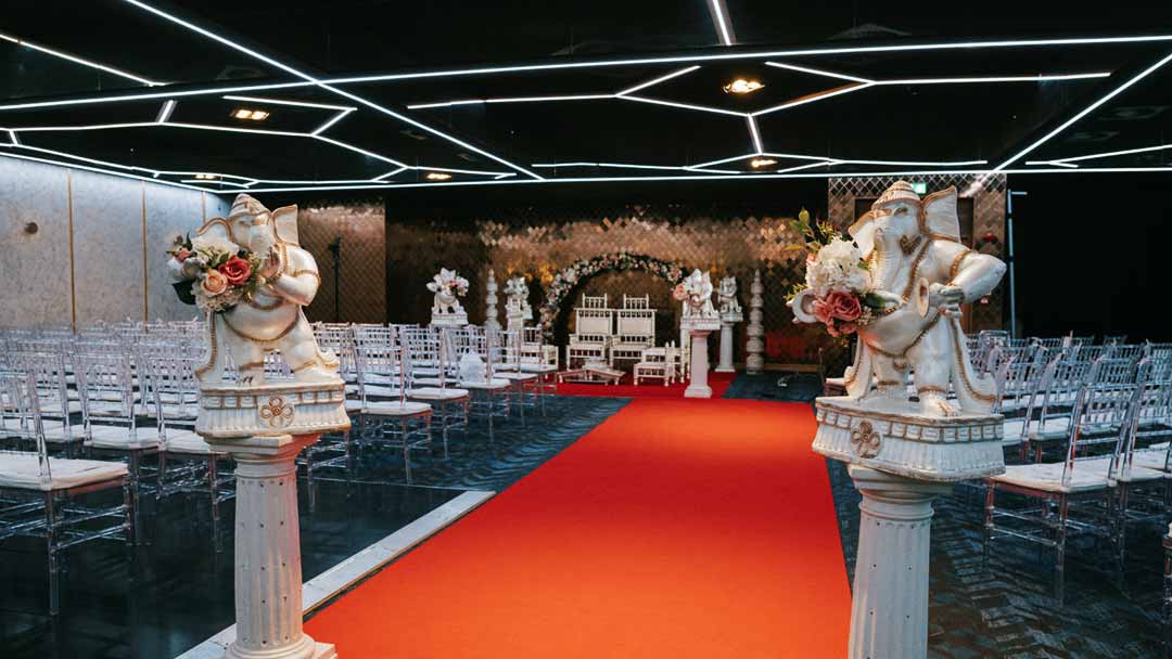An indoor Rose Garden venue, set up for a Hindu wedding ceremony. In the foreground, there are two white Ganpati statues. 