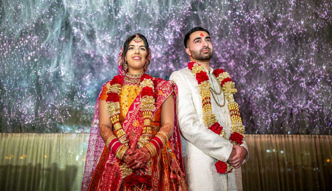 A Hindu couple, dressed in traditional Indian attire, stands against a vibrant purple backdrop in Rose Garden Wolverhampton. 