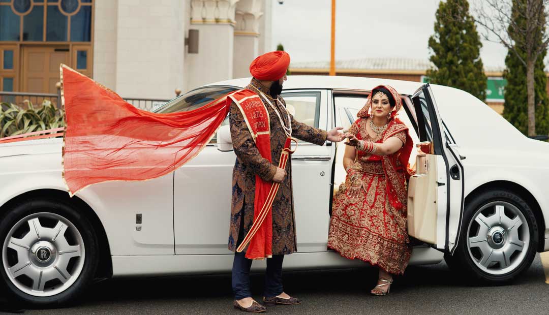 Leamington Gurdwara car park wedding photoshoot In the Leamington Gurdwara car park, a groom is standing next to a white luxury car. The car has its door open, and the bride is half seated inside.