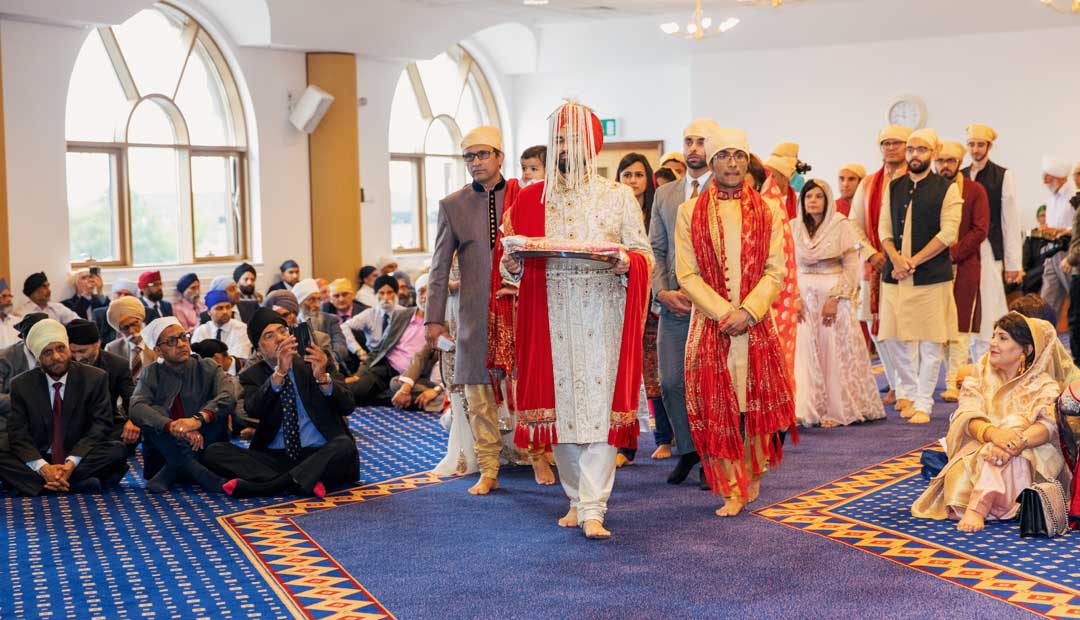 At Gurdwara Sahib Leamington, guests sit on the floor and watch as the groom walks down the aisle of the Darbar Sahib.